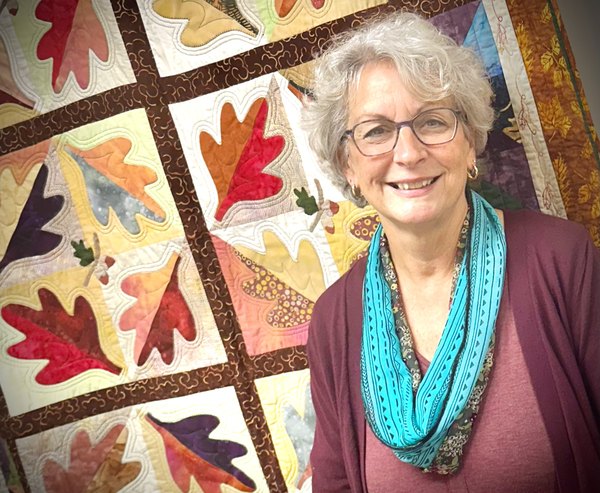 Julie, founder of Sewfunn Dandelion Lessons, standing in front of one of her autumn-leaves quilts